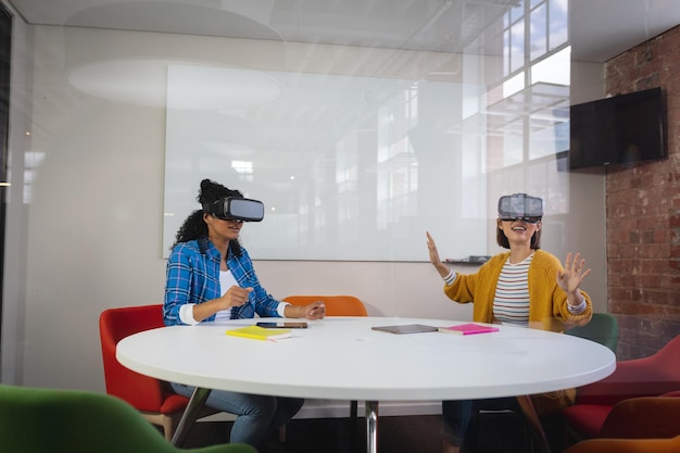 Photo diverse female colleagues sitting at work wearing virtual reality set and playing