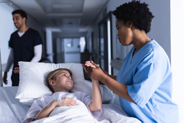 写真 病院の廊下でベッドに横たわっている女の子と話す多様な女性医師