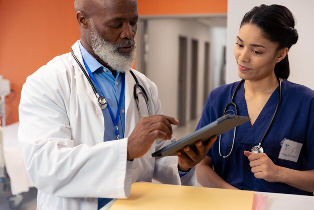 Photo diverse female and senior male doctor using tablet and talking in hospital ward, copy space. hospital, medical and healthcare services.