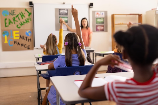 Foto diverse insegnanti e studenti delle scuole elementari alzano le mani in classe