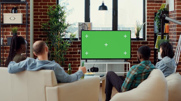 Diverse friends watching tv series on greenscreen template,
using isolated mockup copyspace to watch movie or film on
television. looking at isolated chroma key background. tripod
shot.