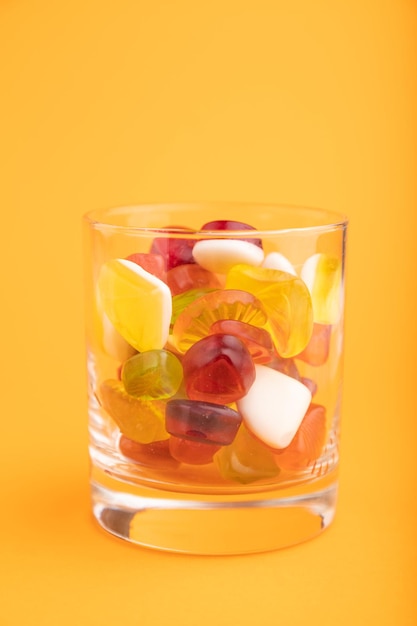 Diverse fruit gelei snoepjes in drinkglas op oranje achtergrond close-up zijaanzicht