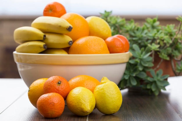 Diverse fruits all citrus in front of a fruit bowl filled with citrus and bananas