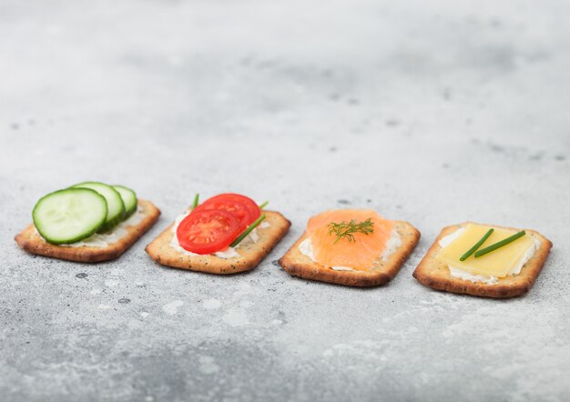 Diverse gezonde crackers met zalm en kaas, tomaat en komkommer op lichte keukentafel