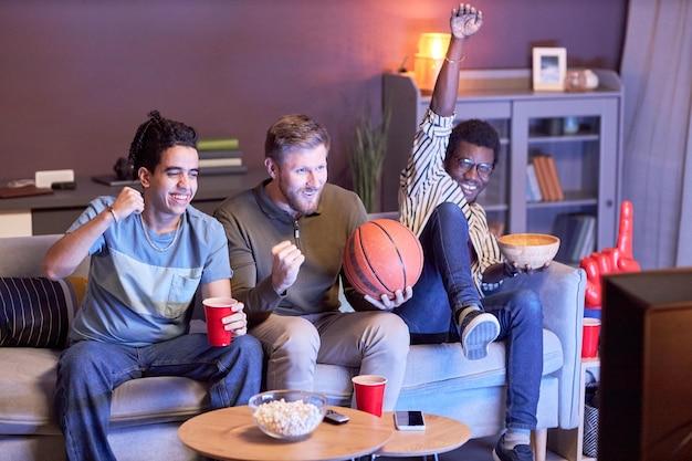 Diverse groep emotionele sportfans die thuis naar basketbalwedstrijden kijken