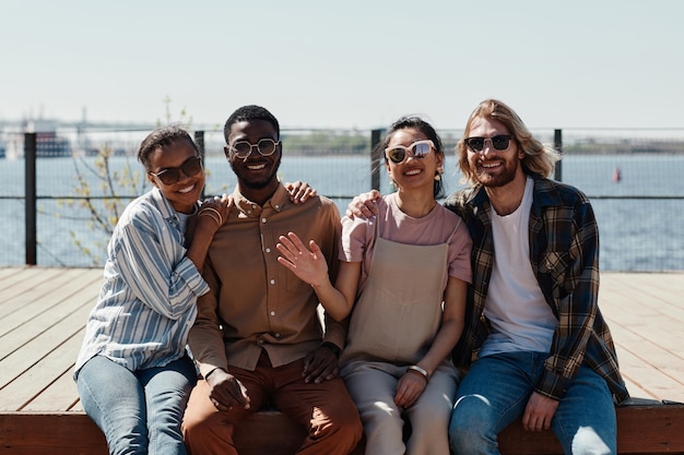 Diverse groep jonge mensen die naar de camera glimlachen terwijl ze buiten bij de rivier poseren, allemaal met een zonnebril