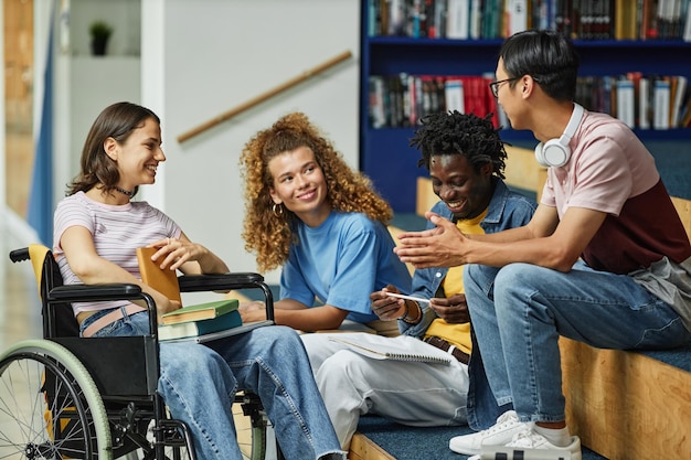 Diverse groep jongeren die chatten in de universiteitsbibliotheek, inclusief vrouwelijke student met een handicap