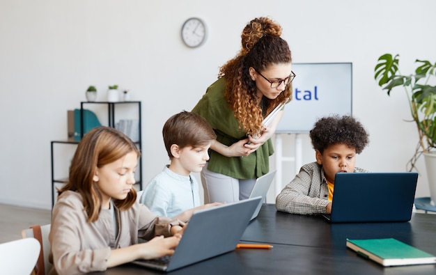 Diverse groep kinderen die computers gebruiken tijdens IT-les op school met jonge vrouwelijke leraar