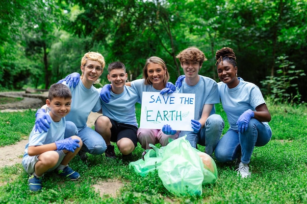 Diverse groep mensen die afval oprapen in het park Vrijwilligerswerk voor de gemeenschap Gelukkige internationale vrijwilligers die een bordje vasthouden met de boodschap 'Save the Earth'
