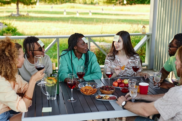 Diverse groep vrienden die in de zomer buiten aan tafel zitten te raden wie er speelt