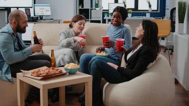 Diverse groep werknemers rammelende kopjes en flessen bier om te vieren in vrije tijd na het werk. Collega's genieten van drankjes samen op kantoor met snacks en alcoholische drank.