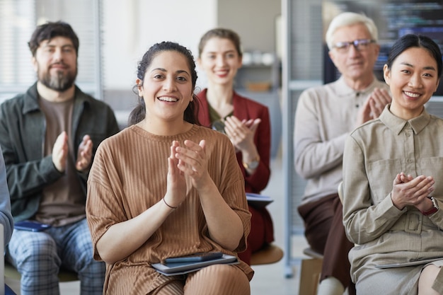 Diverse group of business people applauding while sitting on chairs in audience at meeting or seminar