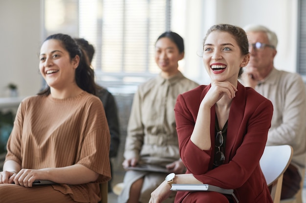 Diverse group of business people sitting on chairs in audience and listening at meeting or seminar, focus on two smiling businesswomen in foreground