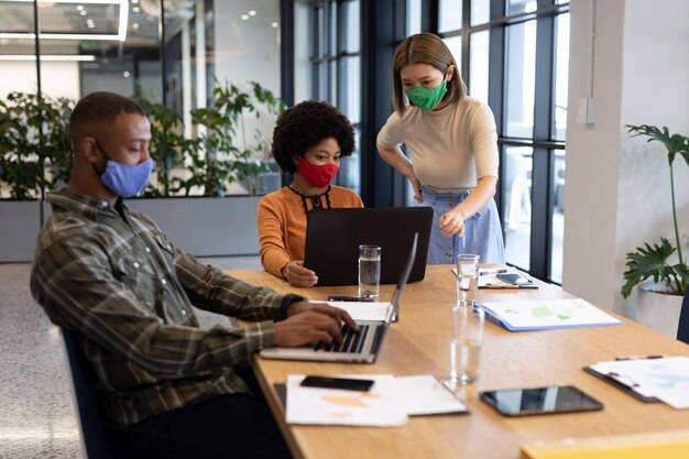 Photo diverse group of business people working in creative office. group of people wearing face masks and using laptops. social distancing protection hygiene in workplace during covid 19 pandemic.