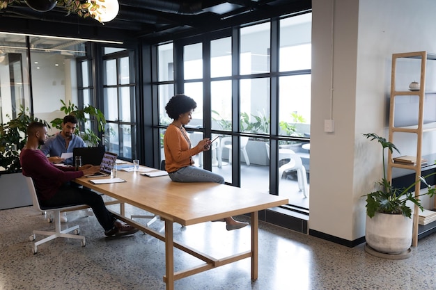 Diverse group of business people working in creative office. woman sitting on a table and using tablet. business people and work colleagues at a busy creative office.
