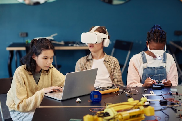 Photo diverse group of children building robots in engineering class and using vr technology