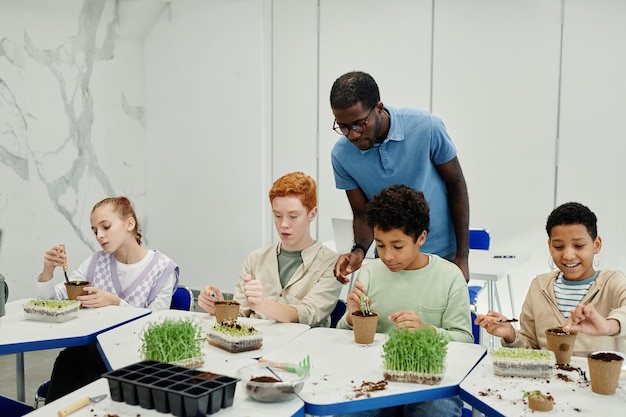 Diverse group of children planting seeds while experimenting at biology class in school with African-American teacher supervising