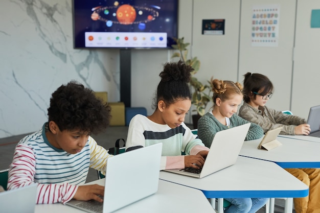 Diverse group of children sitting in row at school classroom and using computers