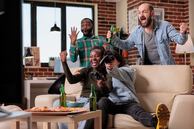 Diverse group of friends celebrating video games win together, playing competition at party gathering with alcohol. People feeling happy about victory and winning, drinking beer at home.