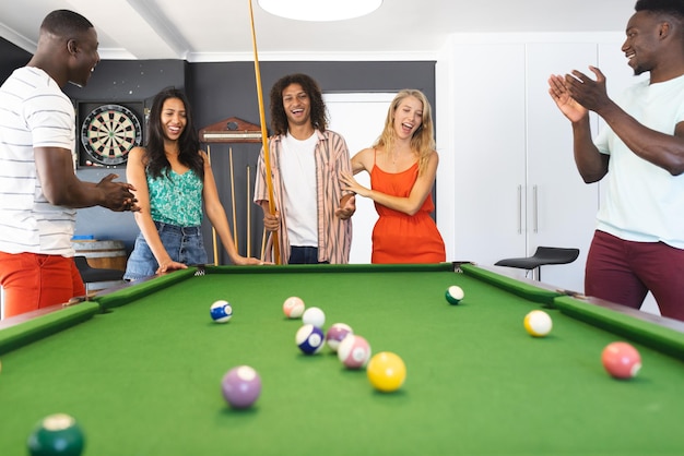 Diverse group of friends enjoys a game of pool with a young biracial woman taking her shot