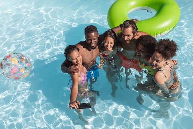 Diverse group of friends having fun and taking selfie in swimming pool. hanging out and relaxing outdoors in summer.