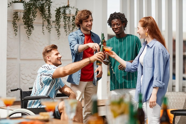 Gruppo eterogeneo di amici tra cui una persona in sedia a rotelle che brinda con un drink mentre si gode la festa