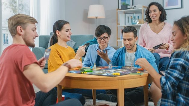 diverse group of guys and girls playing in a strategic board game with cards and dice reading cards and laughing friends having fun cozy living room in a daytime