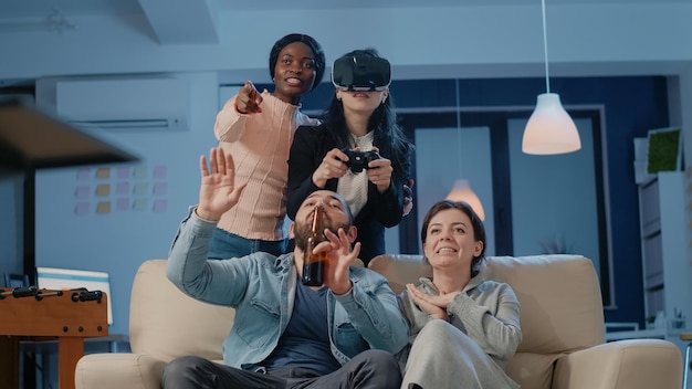 Diverse group of people playing video games with vr glasses and\
controller after work to do fun activity. workmates enjoying game\
play with television on console and joystick at office