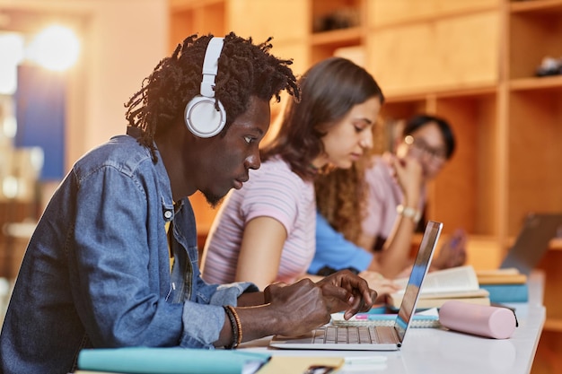 Diverse group of students in row using laptops and studying in college library focus on black young