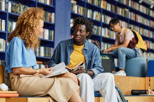 図書館のラウンジで勉強している学生の多様なグループは、女性のフライと話している黒人の若い男性に焦点を当てています