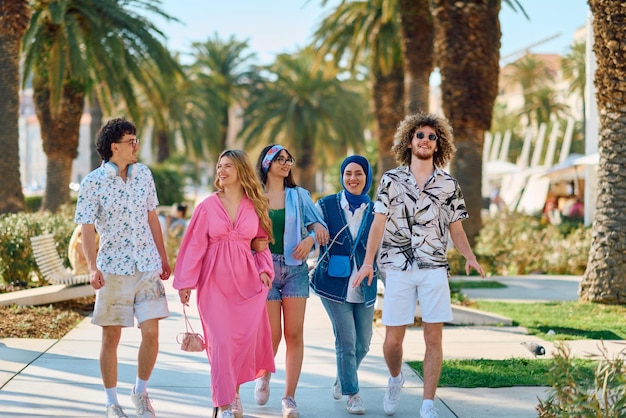 Разнообразная группа туристов, одетых в летнюю одежду, прогуливается по туристическому городу с широкими