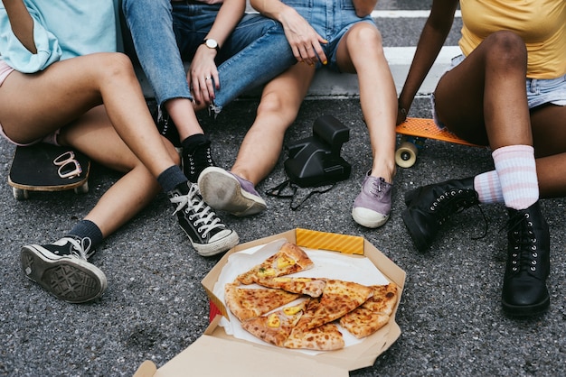 Разнообразные группы женщин, сидя на полу, едят пиццу вместе