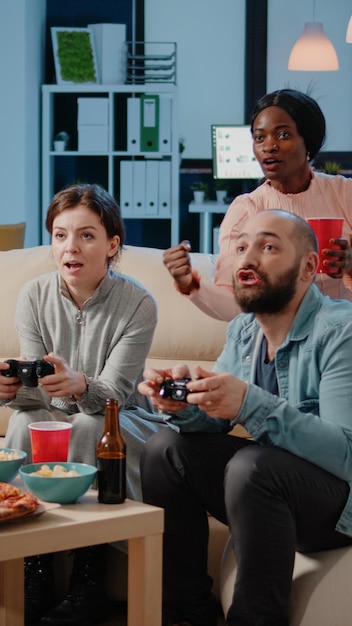 Diverse group of workmates using joysticks to play video games\
on television. colleagues cheering while playing game with\
controllers on tv console to have fun and entertainment.