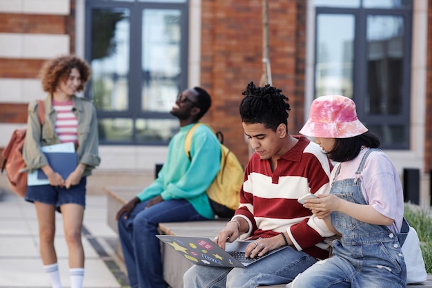 대학 캠퍼스 밖에서 줄지어 앉아 노트북 복사 공간으로 공부하는 젊은 학생들의 다양한 그룹