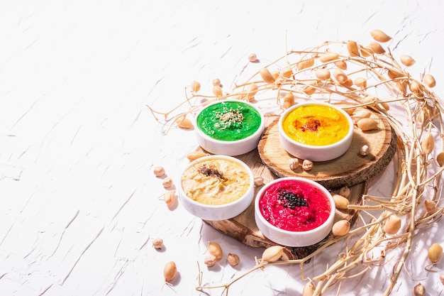 Diverse hummus dips, de platte hummus in verschillende kleuren met spinazie, rode biet, kurkuma en groenten, vegan snack. Witte stopverfachtergrond, kopieer ruimte