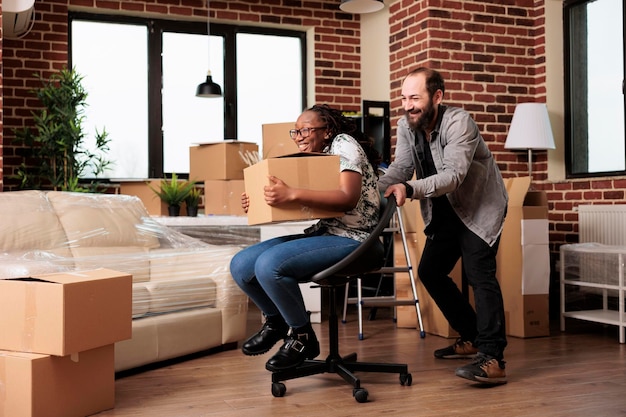 Diverse husband and wife having fun relocating in new household bought on mortgage loan to move in together. Enjoying moving day with furniture in first real estate owned, new beginnings.