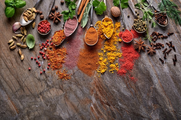 Diverse kleurrijke kruiden en specerijen in lepels om te koken: kurkuma, dille, paprika, kaneel, saffraan, basilicum en rozemarijn. Indiase kruiden. Op oude steen bruine achtergrond. Bovenaanzicht.