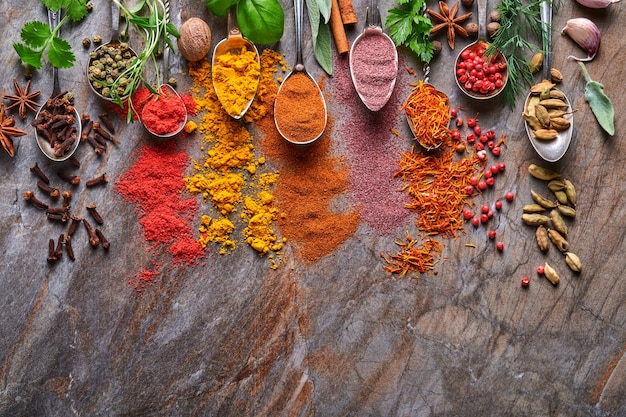 Diverse kleurrijke kruiden en specerijen in lepels om te koken: kurkuma, dille, paprika, kaneel, saffraan, basilicum en rozemarijn. Indiase kruiden. Op oude steen bruine achtergrond. Bovenaanzicht