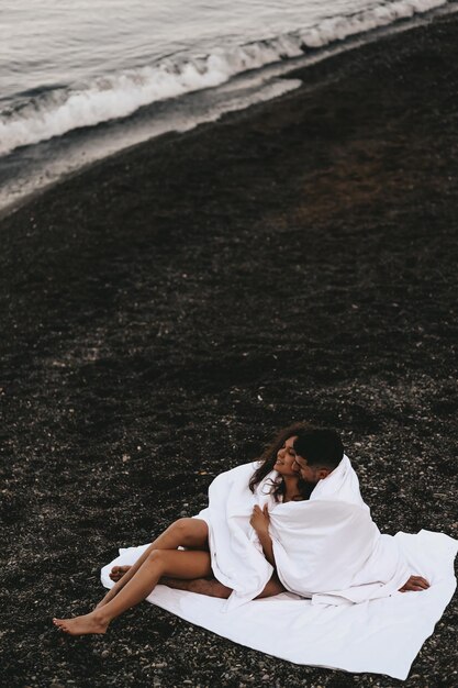 Photo a diverse of lovers a man and a woman embrace under a blanket on the ocean at night outdoor