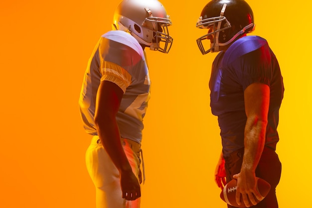 diverse male american football players holding ball with neon orange lighting