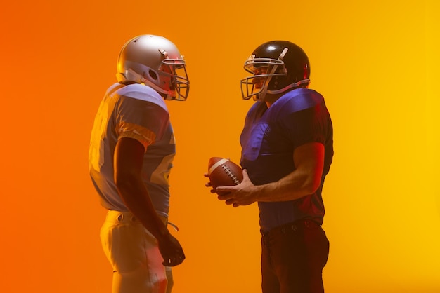 diverse male american football players holding ball with neon orange lighting