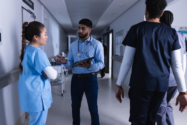 Photo diverse male and female doctors talking and using tablet in hospital corridor