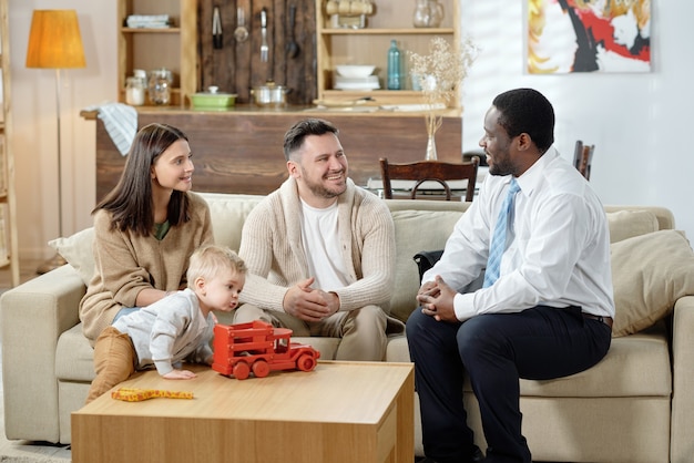 Diverse man en gelukkige familie met jongen die onroerende goederenoverleg hebben die samen op bank zitten