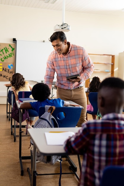 Foto diverse mannelijke leraren met tablets en basisschoolkinderen die aan tafels in de klas zitten