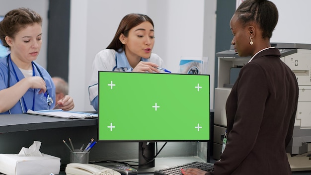 Diverse medical staff working with greenscreen on computer at\
hospital reception counter. using isolated copyspace template with\
blank mockup background and chroma key display on monitor.