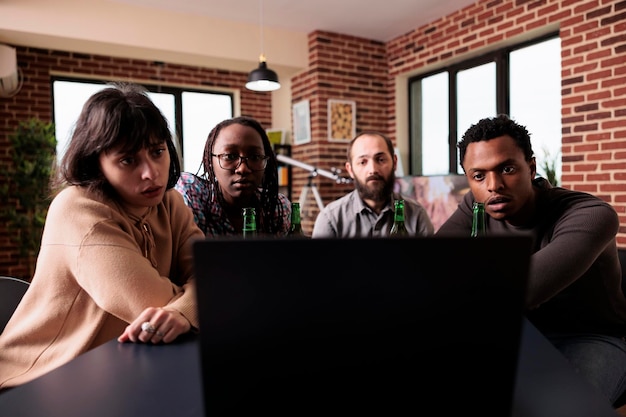 Diverse mensen zitten aan tafel in de woonkamer terwijl ze samen naar dramafilms kijken op een laptopcomputer. Multiraciale groep vrienden die thuis zitten terwijl ze genieten van spannende films.