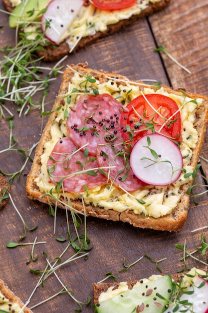 Diverse mini sandwiches met roomkaas, groenten en salami. Broodjes met komkommer, radijs, tomaten, salami op een grijze achtergrond, bovenaanzicht. Plat leggen.