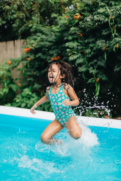 diverse mixed race toddler girl at home having fun in kiddie pool in backyard being very happy