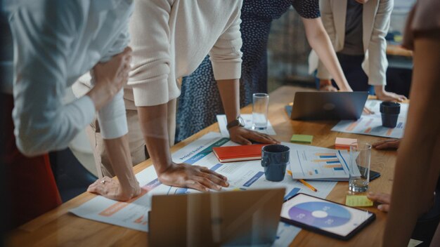 Diverse Multi Ethnic Team of Professional Businesspeople Meeting in the Modern Office Conference Room Creative Team Gathers Around Table to Discuss App Design Analyze Data Focus on Desk and Hands