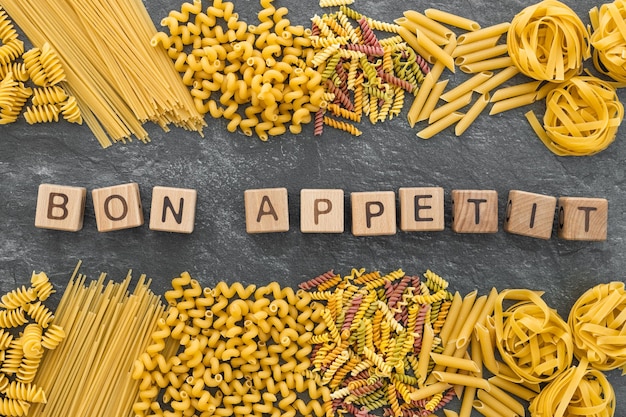 Diverse pasta en woord bon appetit geschreven houten kubussen op donkere stenen achtergrond